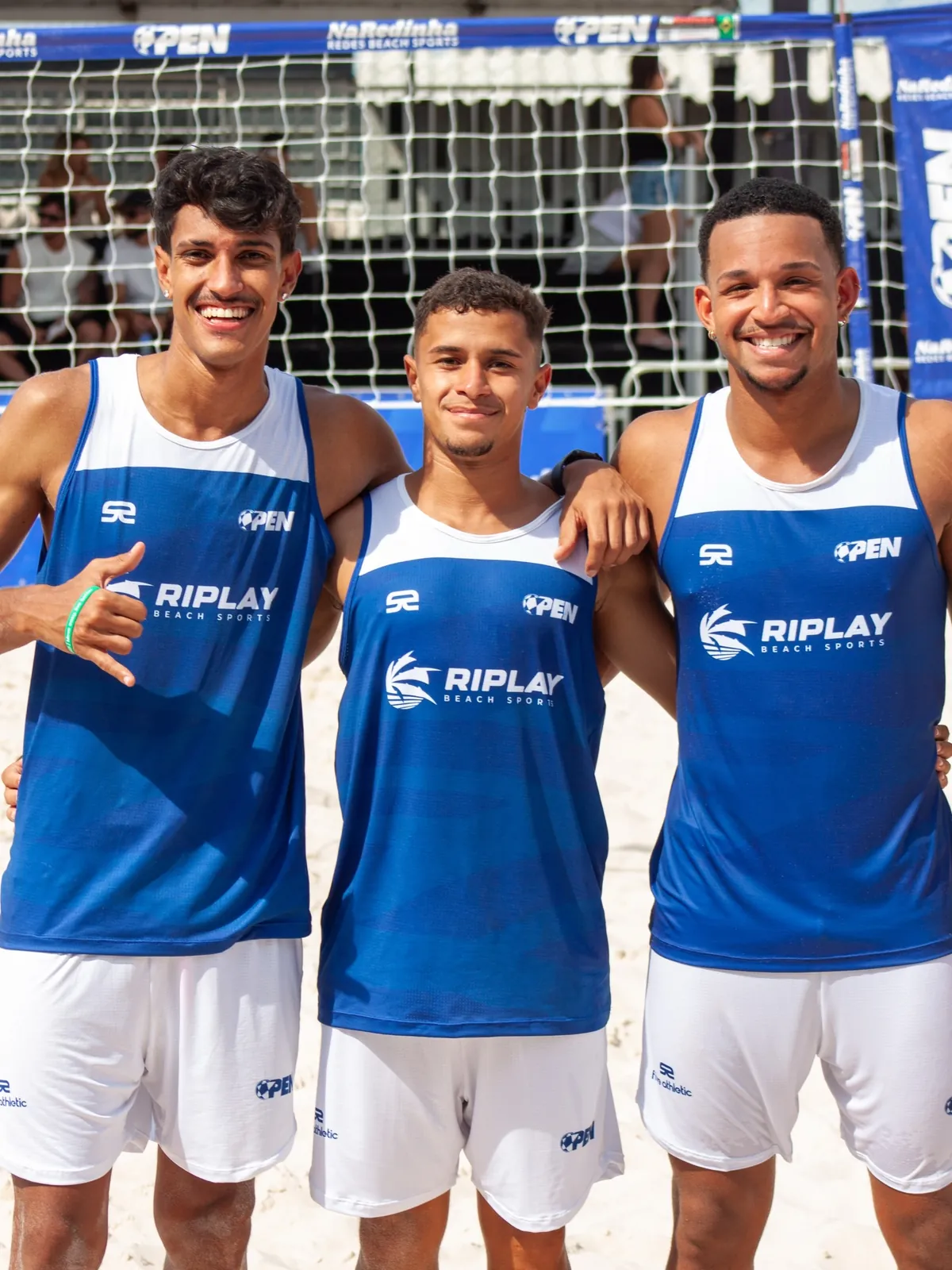 Três atletas abraçados sorrindo na arena do OPEN