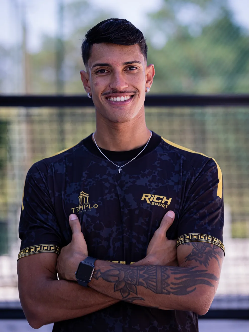 Matox sorrindo de braços cruzados, com o uniforme da Templo